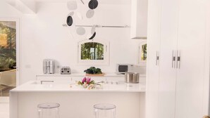 Une cuisine moderne avec un plan de travail blanc, des appareils en acier inoxydable et une fenêtre donnant sur un paysage verdoyant.