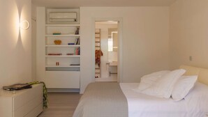 Une chambre à coucher comprenant un lit, une table de chevet, une armoire et une porte ouverte donnant sur une salle de bain.