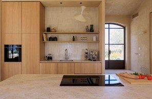 A modern kitchen with wooden cabinets, a built-in oven, a countertop with a kettle, and a window with a view. - 4BR Villa in Noto, Heated Pool (Noto)