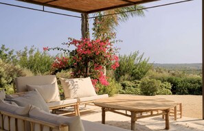 An outdoor seating area with a wooden table and a sofa, surrounded by greenery and a view of the landscape. - 4BR Villa in Noto, Heated Pool (Noto)