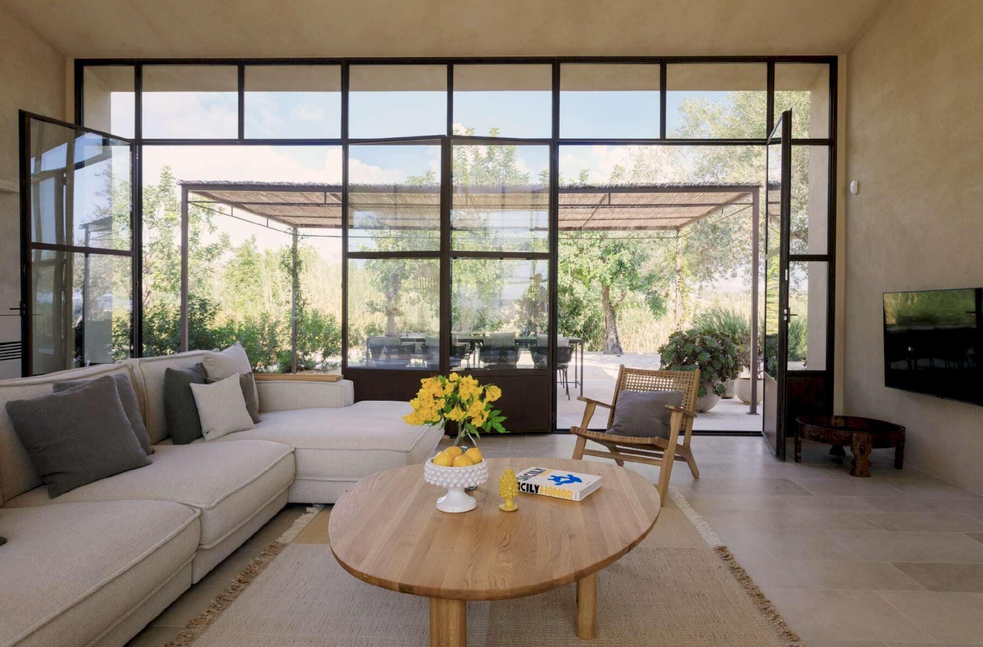 A modern living room with a large window, a sofa, a coffee table with flowers, and a television.