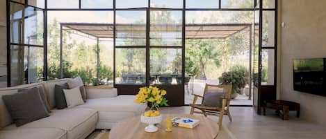 A modern living room with a large window, a sofa, a coffee table with flowers, and a television.