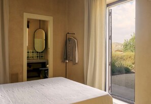 A bedroom with a bed, a bathroom with a mirror and sink, and a view of the outdoors. - 4BR Villa in Noto, Heated Pool (Noto)