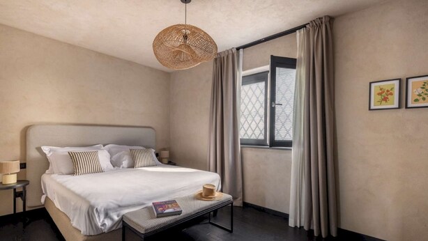 A hotel room with a large bed, a bedside table with a lamp, a window with curtains, and two framed pictures on the wall. - Elegant 4 Bedroom Private Pool Villa in Acireale (Acireale)