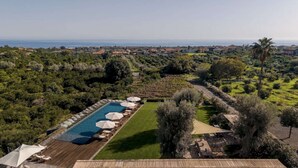 A pool with lounge chairs and umbrellas, surrounded by greenery and a view of the sea. - Elegant 4 Bedroom Private Pool Villa in Acireale (Acireale)