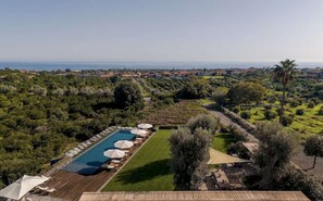 A pool with lounge chairs and umbrellas, surrounded by greenery and a view of the sea. - Elegant 4 Bedroom Private Pool Villa in Acireale (Acireale)