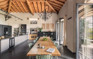 A modern kitchen with a wooden ceiling, a dining area with a long table, and a view through a glass door. - Elegant 4 Bedroom Private Pool Villa in Acireale (Acireale)