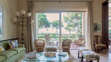 A spacious living room with a glass coffee table, wicker chairs, a sofa, and a view of a garden through large sliding doors.
