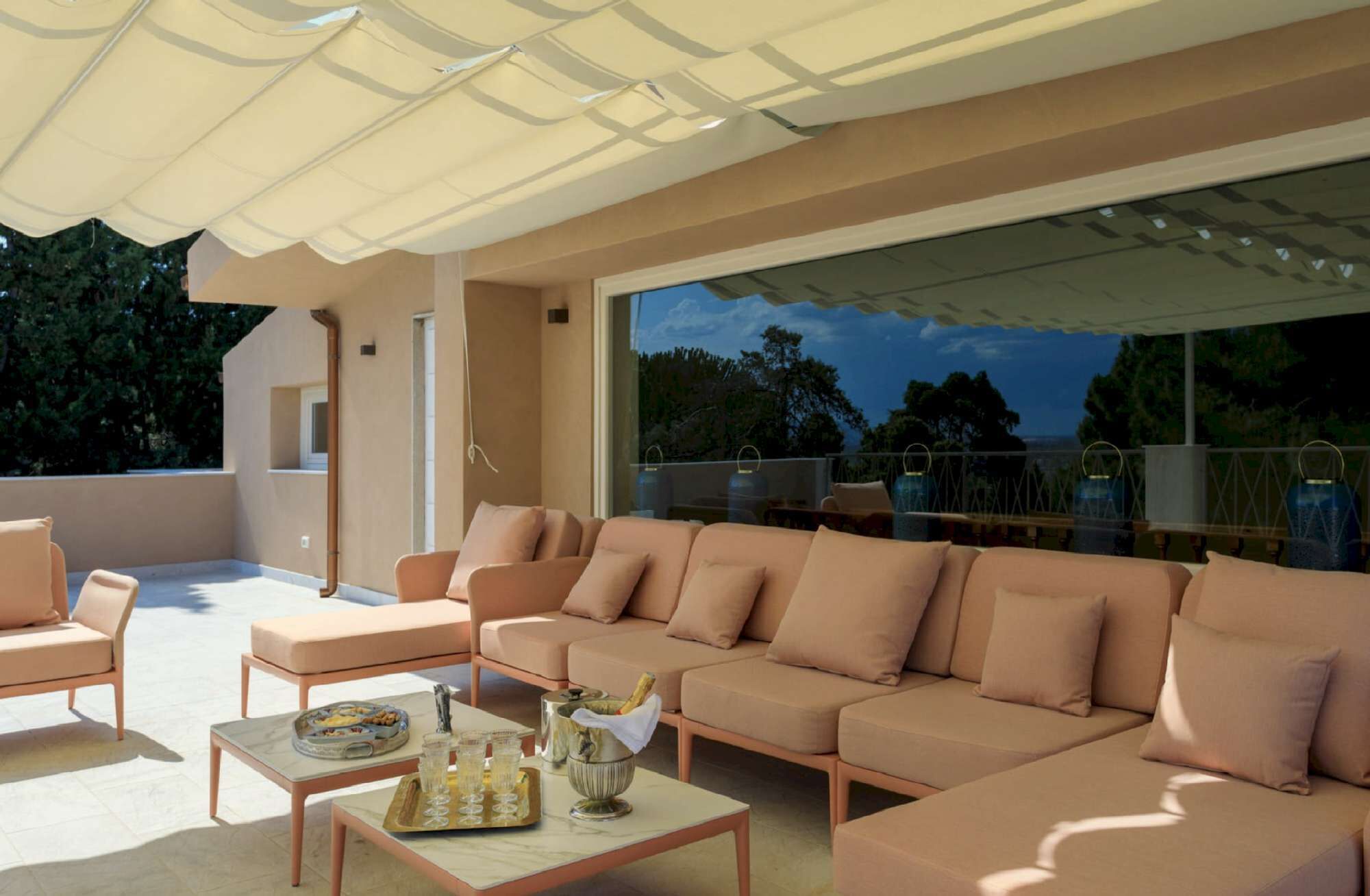 A modern outdoor seating area with a sofa and chairs, a table with drinks, and a view of the outdoors.