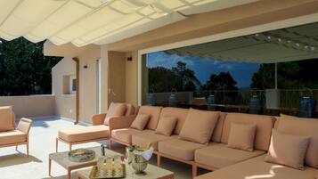 A modern outdoor seating area with a sofa and chairs, a table with drinks, and a view of the outdoors.