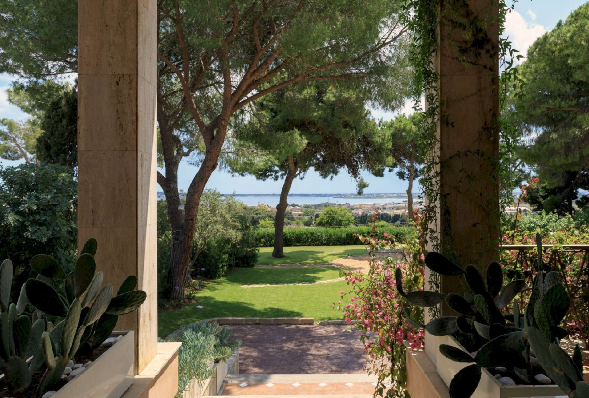 A garden pathway leading to a lawn with trees and a view of the sea.