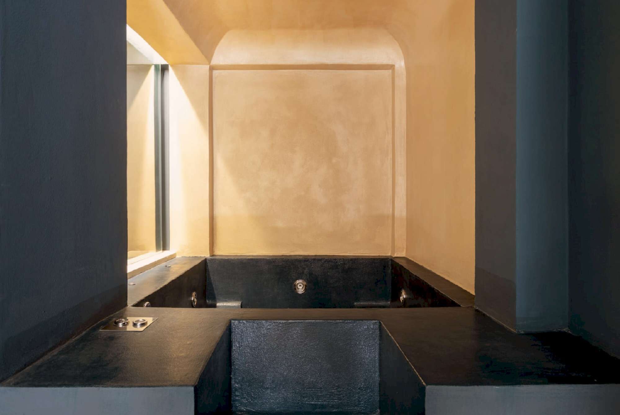 A modern bathroom with a minimalist design, featuring a bathtub, a shower area, and a large window providing natural light.