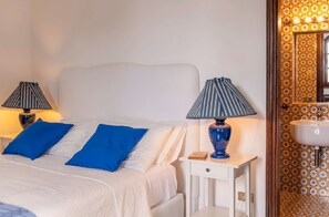 Ein Hotelzimmer mit einem Bett, zwei Nachttischlampen, einem Nachttisch, einer Schublade und einem Badezimmer mit Waschbecken und Spiegel.