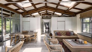 A spacious interior with a high ceiling, a dining area with a table and chairs, a sofa, and a window with a view. - Large Orbetello Villa with Private Pool (Orbetello)