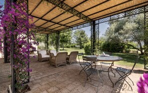 Eine Terrasse im Freien mit Korbmöbeln, einem runden Tisch und einer Pergola.
