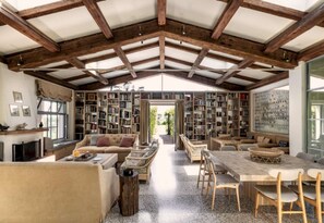 A spacious room with a high ceiling, exposed wooden beams, a large bookshelf, a fireplace, and a dining area with a table and chairs. - Large Orbetello Villa with Private Pool (Orbetello)