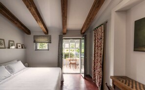 A bedroom with a bed, a window, a door leading to an outdoor area, and a wooden bench. - Large Orbetello Villa with Private Pool (Orbetello)