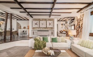 A modern living room with a white sofa, a coffee table with candles, and a stone fireplace. - Sardinia Dream Getaway: 4BR Villa with Pool & Garden (Santa Margherita di Pula)