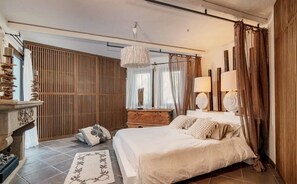 A bedroom with a bed, a wooden wardrobe, a nightstand, a decorative lamp, and a window with curtains. - Sardinia Dream Getaway: 4BR Villa with Pool & Garden (Santa Margherita di Pula)