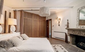 Ein Schlafzimmer mit Bett, Nachttischlampen, einer Wand aus Holzlatten, einem Kamin und einem Spiegel.