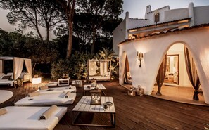 Eine gut beleuchtete Außenpatio-Terrasse mit Liegestühlen, Tischen und einem überdachten Sitzbereich.