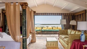 A luxurious bedroom with a canopy bed, a green sofa, a red table, and a view of the sea. - Stunning 7BR Villa in Noto with Sea View (Noto)