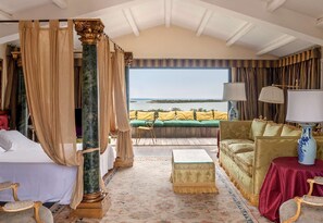 Ein luxuriöses Schlafzimmer mit Himmelsbett, einem grünen Sofa, einem roten Tisch und Meerblick.
