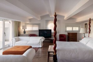 Ein Hotelzimmer mit Himmelbett, Fernseher, rotem Sessel und Holzschrank.