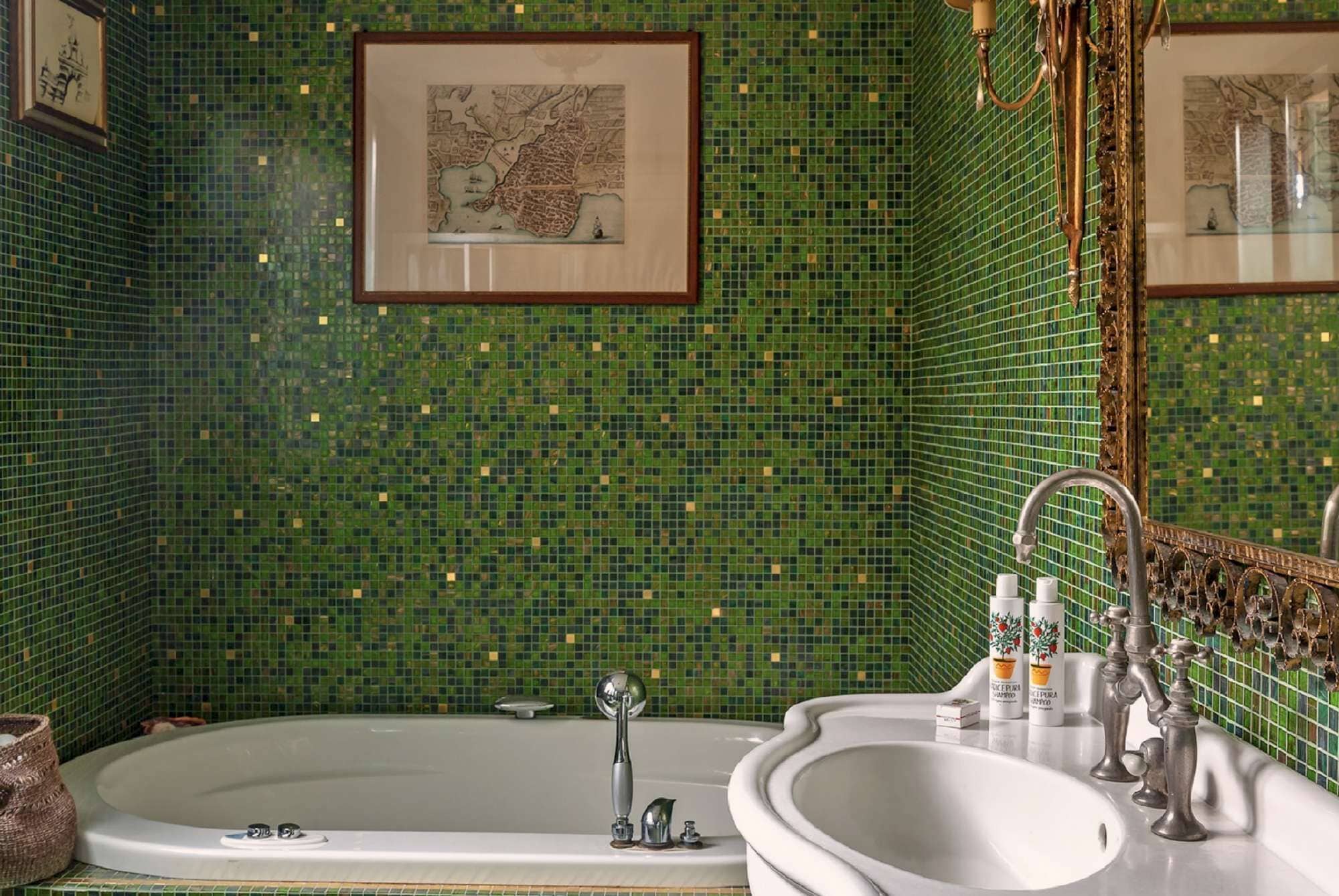 Ein Badezimmer mit grüner Mosaikwand, einer Badewanne, einem Waschbecken und einem Spiegel mit einer Karte.