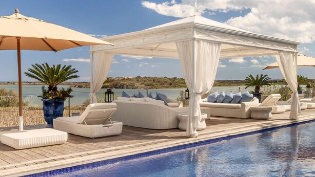 A poolside area with a canopy, lounge chairs, and a view of the water. - Stunning 7BR Villa in Noto with Sea View (Noto)