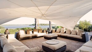 A covered outdoor seating area with wicker furniture and a view of the water. - Stunning 7BR Villa in Noto with Sea View (Noto)
