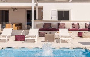 Ein Poolbereich mit Liegestühlen, einem Wasserspiel und einem Gebäude mit Fenster und Rollläden.