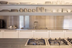Une cuisine moderne dotée d’appareils électroménagers en acier inoxydable, de meubles blancs et d’une variété d’assiettes en céramique blanche disposées sur des étagères.