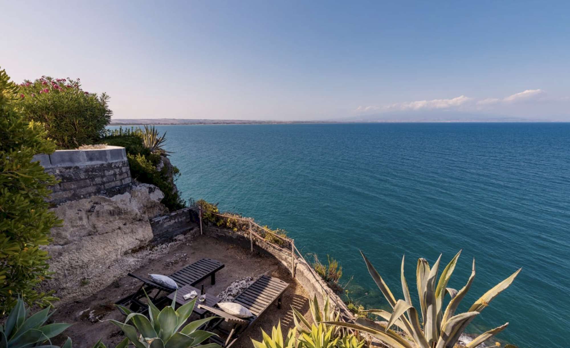 Ein Küsteneigentum mit einer Terrassenfläche, Liegestühlen und Meerblick.