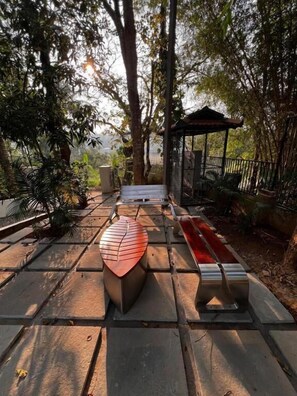 An outdoor seating area with a gazebo, surrounded by trees and a paved walkway.