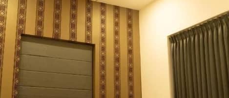 A bedroom with a wooden bed, a headboard, a bedside table, and a curtain.