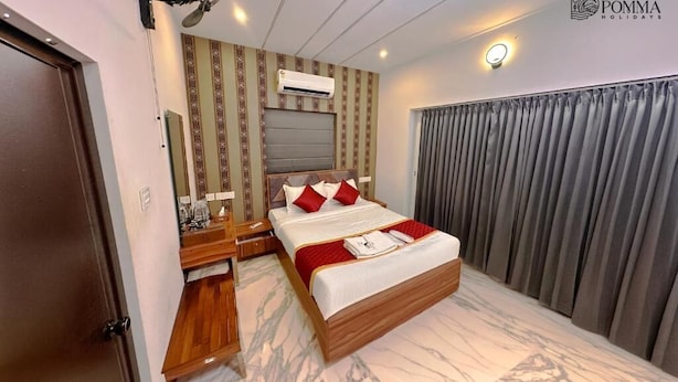 A hotel room with a bed, a desk, a mirror, an air conditioning unit, and a curtain. - Pomma Holidays & Resorts Wayanad (Sulthan Bathery)