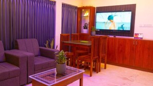 A living room with a sofa, a coffee table, a TV, a dining table with chairs, and a cabinet. - Pomma Holidays & Resorts Wayanad (Sulthan Bathery)