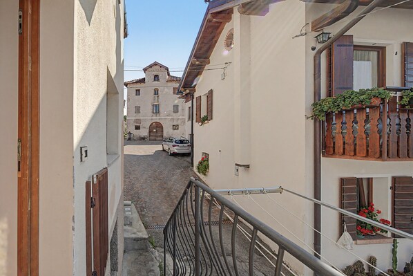 A narrow street with buildings on either side, a car parked on the street, and a staircase leading down to a cobblestone path.