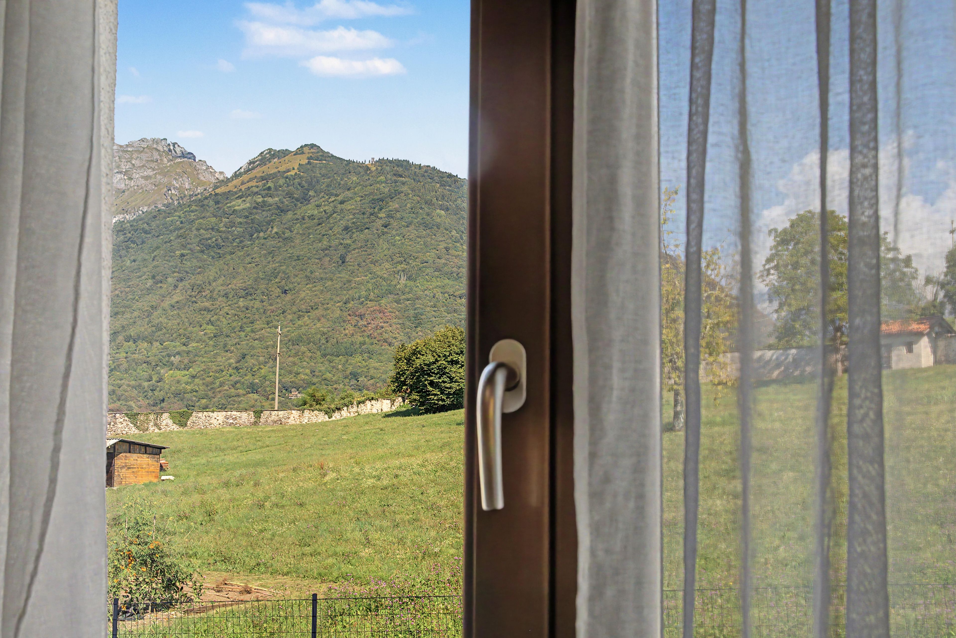 Vista a través de una ventana con un picaporte, que da a un campo verde y una cordillera.