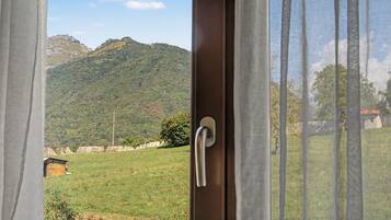 Vista a través de una ventana con un picaporte, que da a un campo verde y una cordillera.