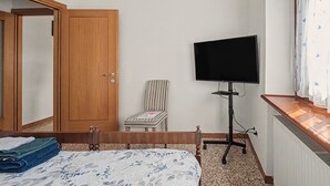 Un dormitorio con una cama, una silla, un televisor sobre un mueble bajo y un armario de madera.