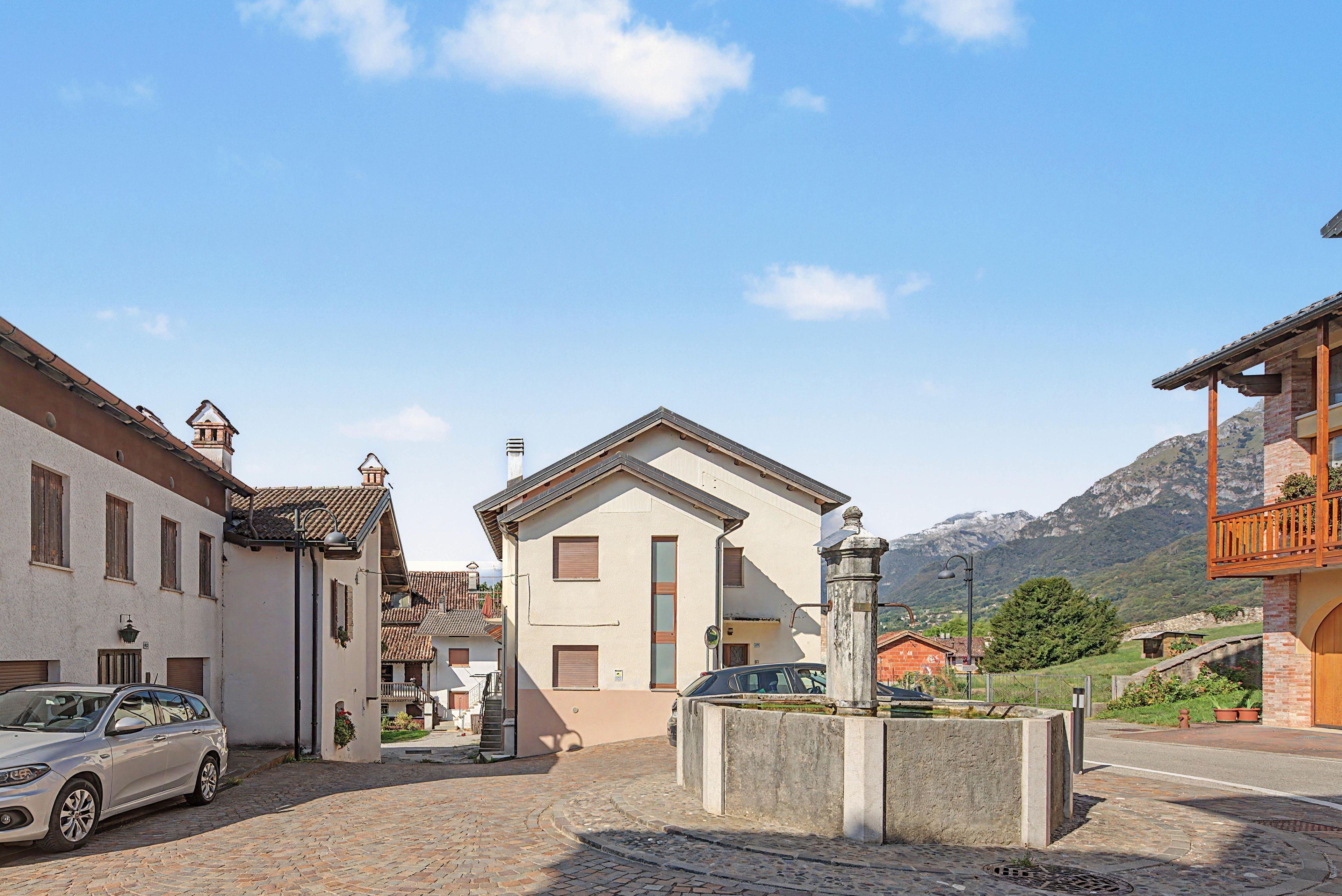 Una calle adoquinada con edificios tradicionales, una fuente y montañas al fondo.