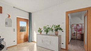 Un pasillo con una puerta de madera, un espejo, una planta en maceta y una mesita con un diseño floral.