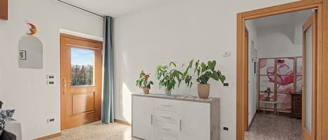 Un pasillo con una puerta de madera, un espejo, una planta en maceta y una mesita con un diseño floral.
