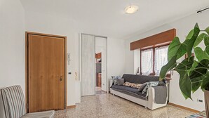 Una habitación con puerta de madera, una silla a rayas, un sofá con cojines estampados y una planta verde grande.
