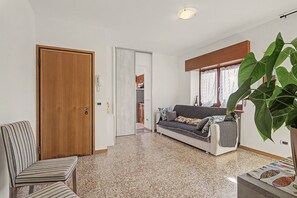 A room with a wooden door, a striped chair, a sofa with patterned cushions, and a large green plant.