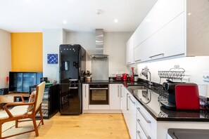 A modern kitchen with a built-in oven, a coffee maker, and a red kettle. - Stylish Angel & Islington Apartment (London)