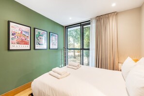 A hotel room with a bed, a window with curtains, and three framed artworks on the wall. - Stylish Angel & Islington Apartment (London)