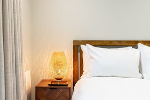 A neatly made bed with white linens, a wooden headboard, and a bedside lamp with a woven shade. - Stylish Angel & Islington Apartment (London)